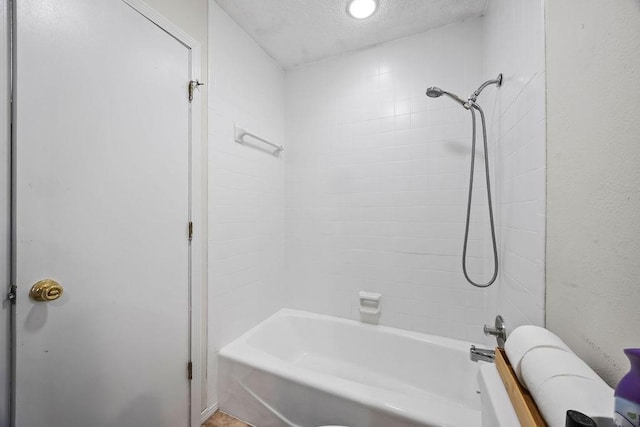 bathroom featuring a textured ceiling and tiled shower / bath