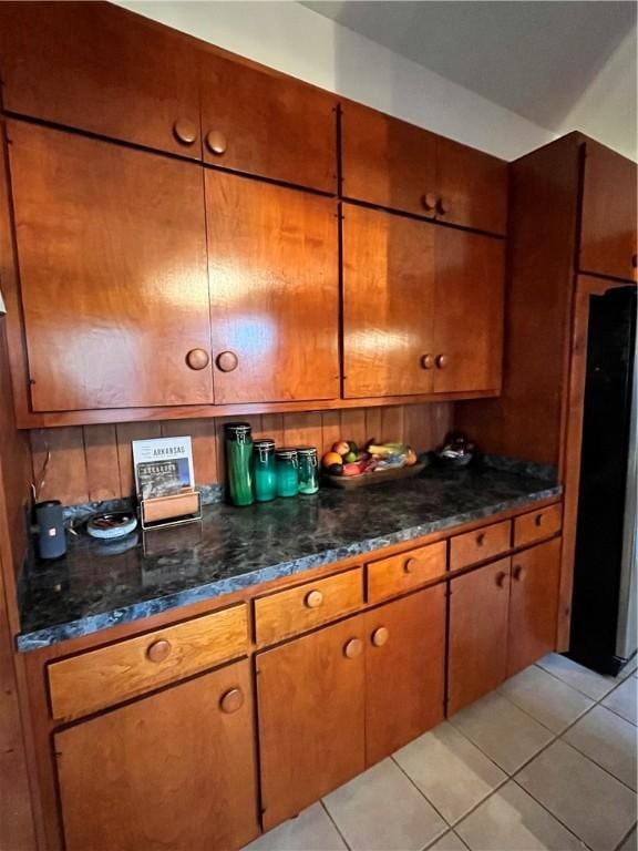 kitchen with brown cabinetry, freestanding refrigerator, decorative backsplash, and light tile patterned floors