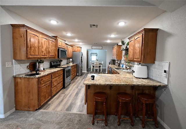 kitchen featuring sink, a kitchen breakfast bar, stainless steel appliances, kitchen peninsula, and decorative backsplash