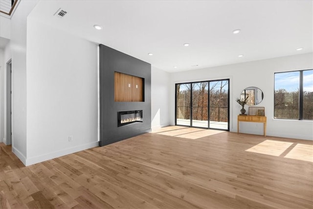 unfurnished living room with plenty of natural light, a large fireplace, and light hardwood / wood-style flooring