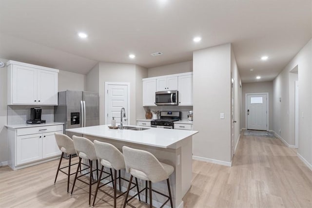 kitchen with light wood-style flooring, a sink, a kitchen breakfast bar, appliances with stainless steel finishes, and an island with sink