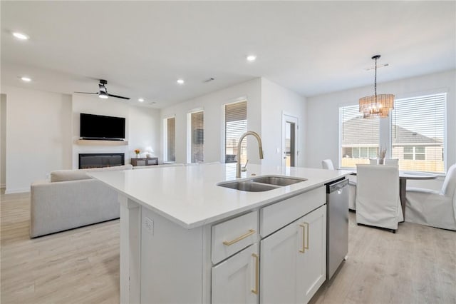 kitchen with a center island with sink, stainless steel dishwasher, pendant lighting, sink, and white cabinetry