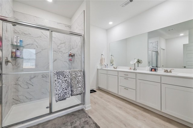 bathroom with hardwood / wood-style floors, a shower with shower door, and vanity