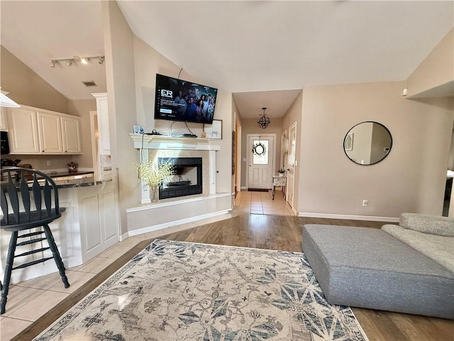 living room with light hardwood / wood-style flooring, a tiled fireplace, vaulted ceiling, and rail lighting