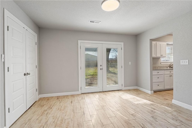 doorway with sink, light hardwood / wood-style floors, french doors, and a textured ceiling