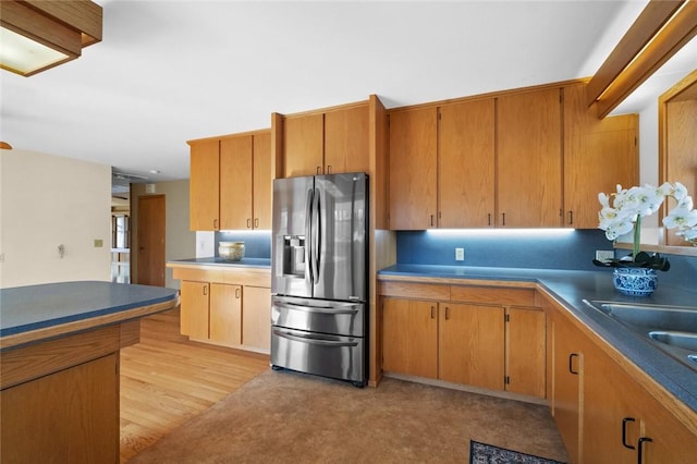 kitchen featuring a sink, stainless steel fridge with ice dispenser, brown cabinets, light wood finished floors, and dark countertops