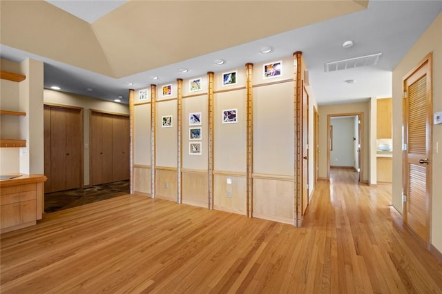 corridor featuring lofted ceiling, light wood finished floors, and visible vents