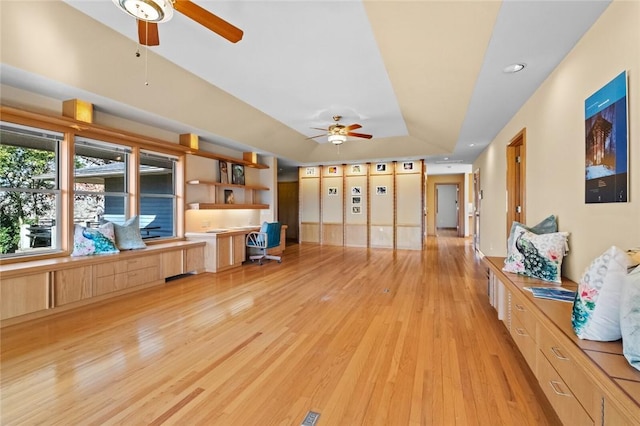 unfurnished living room with light wood-style floors, a raised ceiling, built in study area, and ceiling fan