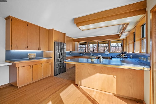 kitchen with a peninsula, a sink, light countertops, stainless steel refrigerator with ice dispenser, and light wood finished floors