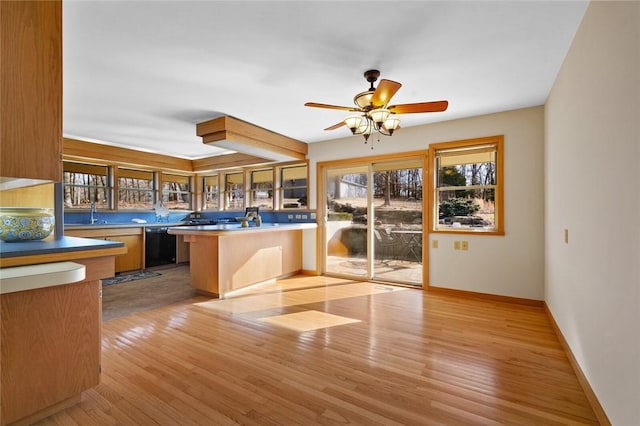 kitchen featuring baseboards, dishwasher, a peninsula, light wood-type flooring, and a kitchen bar