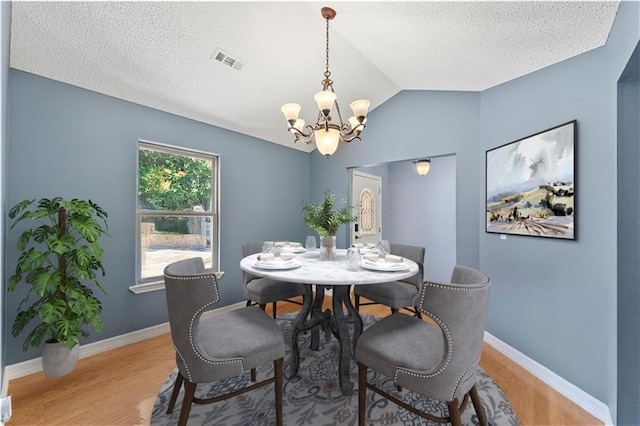 dining area featuring a textured ceiling, hardwood / wood-style flooring, an inviting chandelier, and lofted ceiling