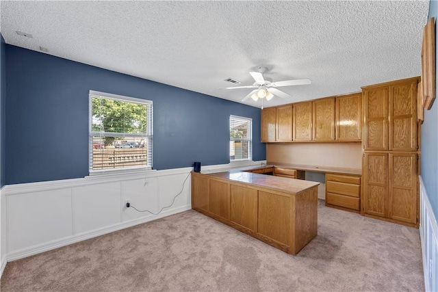 unfurnished office featuring light carpet, ceiling fan, built in desk, and a textured ceiling