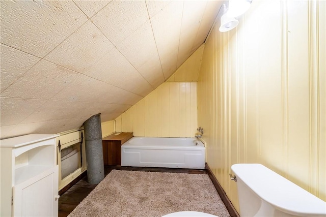 bathroom featuring a bath, lofted ceiling, and wooden walls