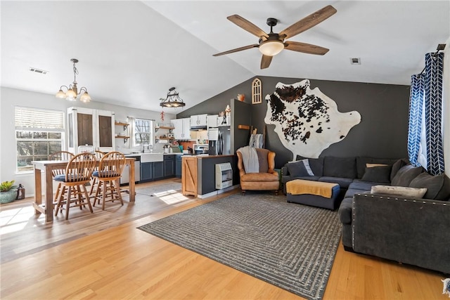 living room featuring sink, ceiling fan with notable chandelier, lofted ceiling, and light hardwood / wood-style flooring