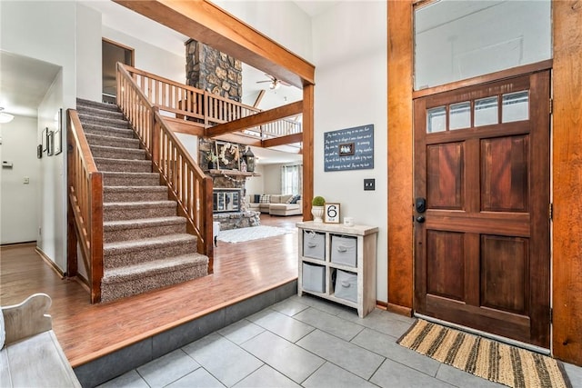 foyer entrance with light tile patterned floors, a ceiling fan, stairway, a high ceiling, and a stone fireplace