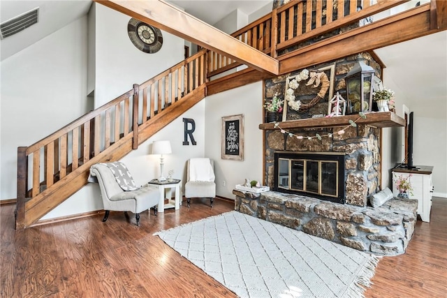 living area featuring a stone fireplace, dark wood-style flooring, a high ceiling, and visible vents