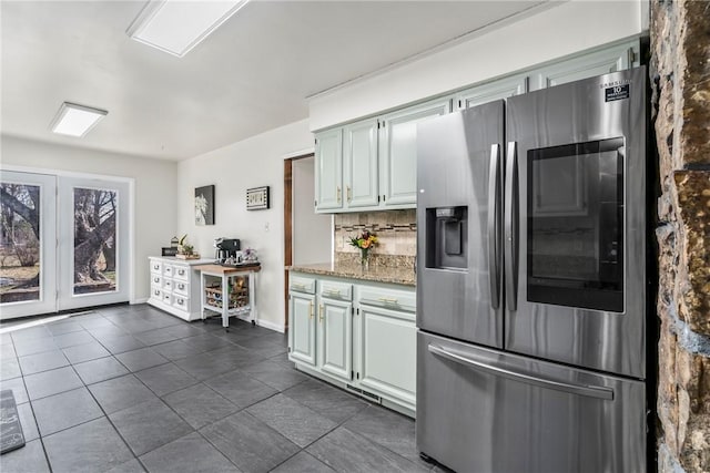 kitchen featuring tasteful backsplash, baseboards, light stone counters, dark tile patterned floors, and stainless steel refrigerator with ice dispenser