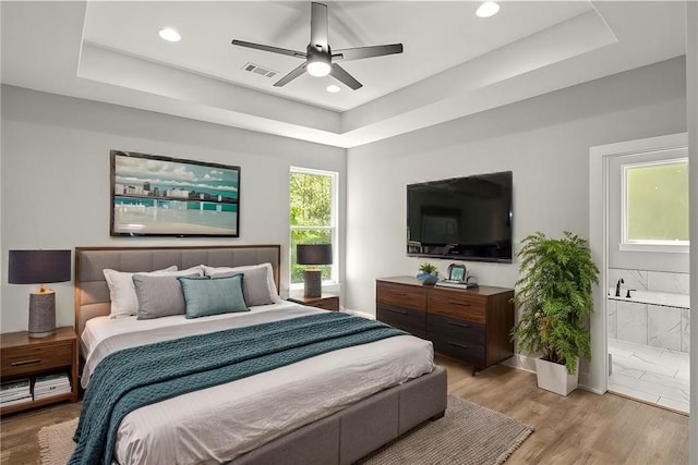 bedroom featuring a tray ceiling, light wood-type flooring, and ensuite bathroom