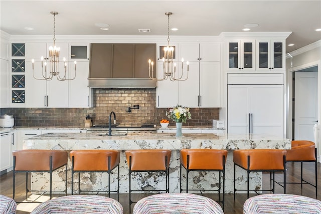 kitchen featuring white cabinetry, a center island with sink, a kitchen breakfast bar, and light stone counters