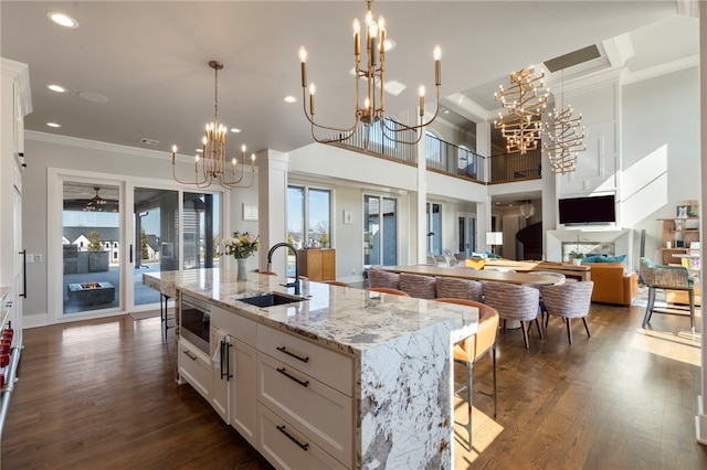 kitchen featuring an island with sink, sink, white cabinets, stainless steel microwave, and a chandelier