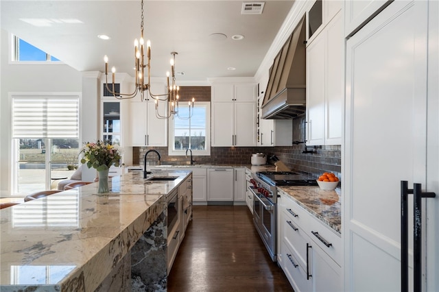 kitchen featuring white cabinetry, decorative light fixtures, double oven range, premium range hood, and light stone counters