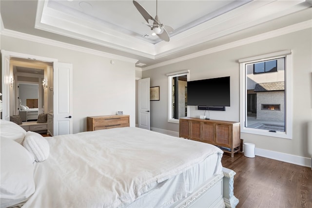 bedroom with ceiling fan, a raised ceiling, a fireplace, dark hardwood / wood-style flooring, and ornamental molding