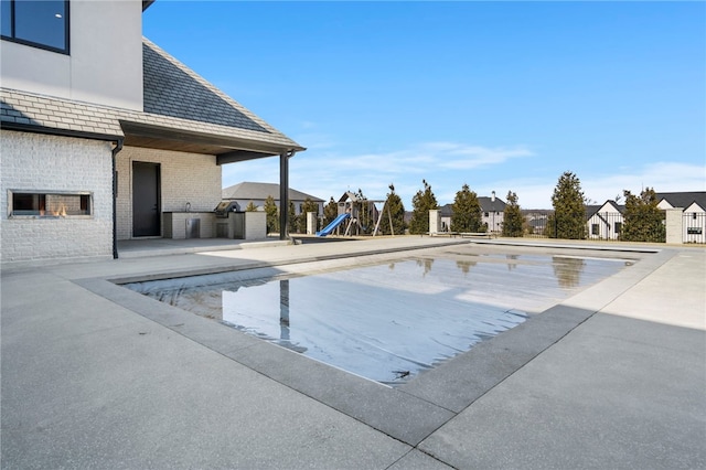 view of pool with a patio, an outdoor kitchen, and a playground