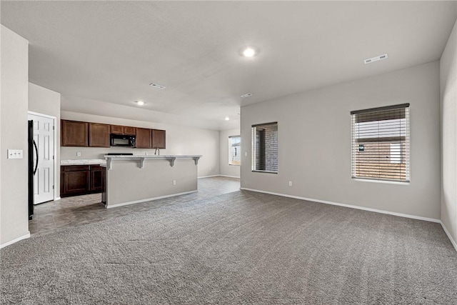 kitchen with a center island with sink, dark brown cabinetry, black appliances, light carpet, and a breakfast bar area