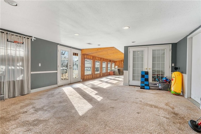 carpeted empty room featuring wooden walls, french doors, a textured ceiling, and baseboards