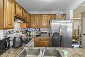 kitchen featuring brown cabinetry, light stone countertops, ventilation hood, black microwave, and stainless steel refrigerator with ice dispenser