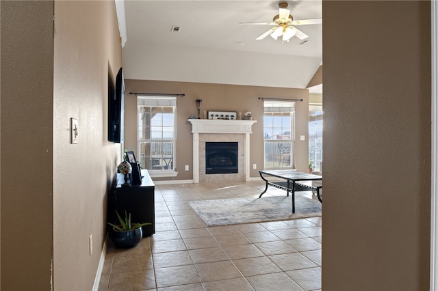 living area featuring light tile patterned floors, baseboards, visible vents, a ceiling fan, and a tiled fireplace