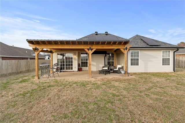 rear view of house featuring a fenced backyard, roof mounted solar panels, a lawn, and a patio