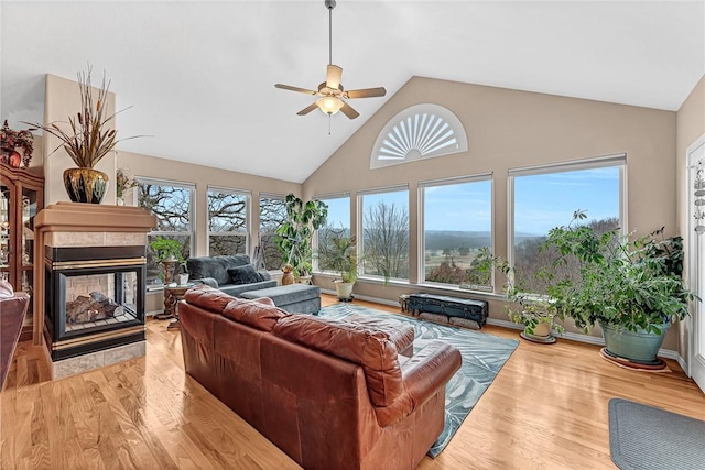 living area featuring light wood-type flooring, ceiling fan, high vaulted ceiling, and a multi sided fireplace