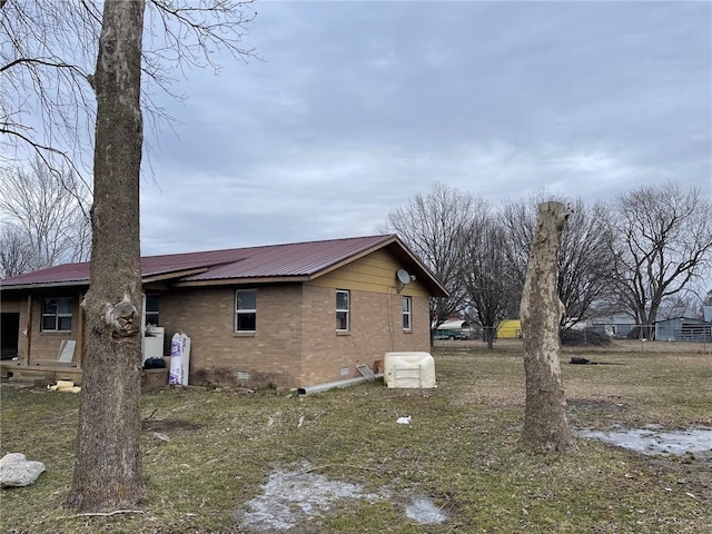 view of side of property with crawl space, brick siding, and metal roof