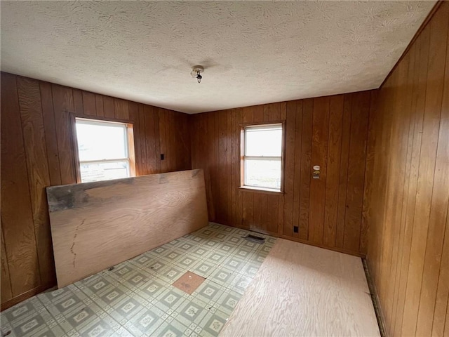 spare room with light floors, wooden walls, visible vents, and a textured ceiling