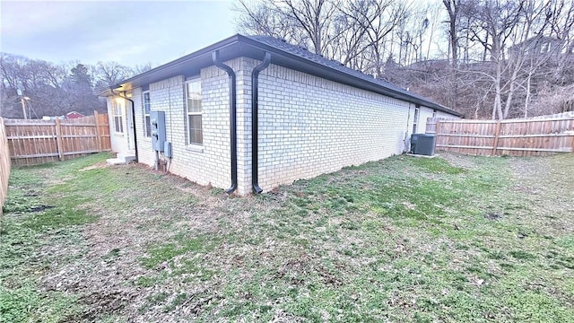 view of property exterior with a fenced backyard, a lawn, central AC, and brick siding