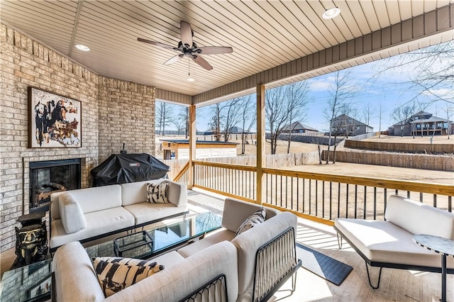 deck featuring ceiling fan, a grill, fence, a patio area, and an outdoor living space with a fireplace