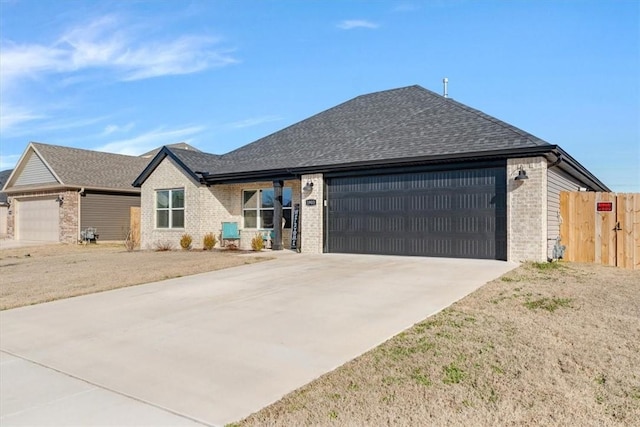 view of front facade featuring an attached garage, brick siding, fence, concrete driveway, and roof with shingles