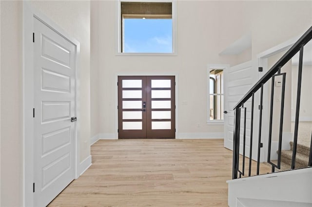 foyer featuring french doors, light wood-style flooring, a high ceiling, stairway, and baseboards