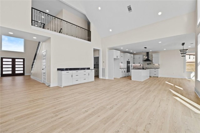 unfurnished living room with recessed lighting, a towering ceiling, visible vents, and light wood-style floors