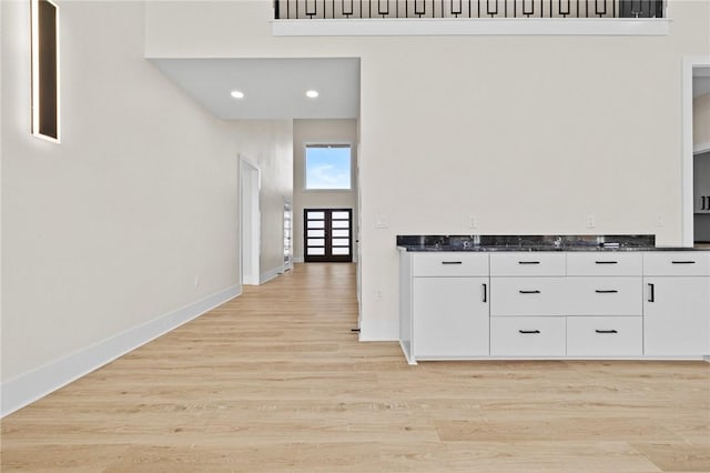 hall with light wood-type flooring, a towering ceiling, baseboards, and recessed lighting