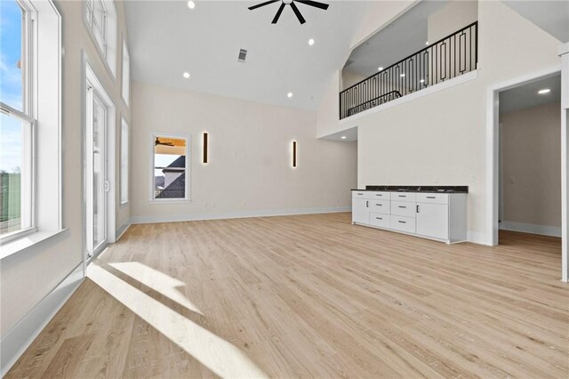 unfurnished living room featuring visible vents, baseboards, light wood-style flooring, ceiling fan, and high vaulted ceiling