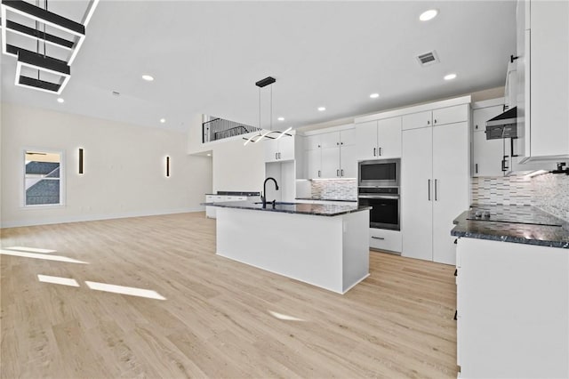 kitchen with dark countertops, appliances with stainless steel finishes, white cabinets, and decorative light fixtures