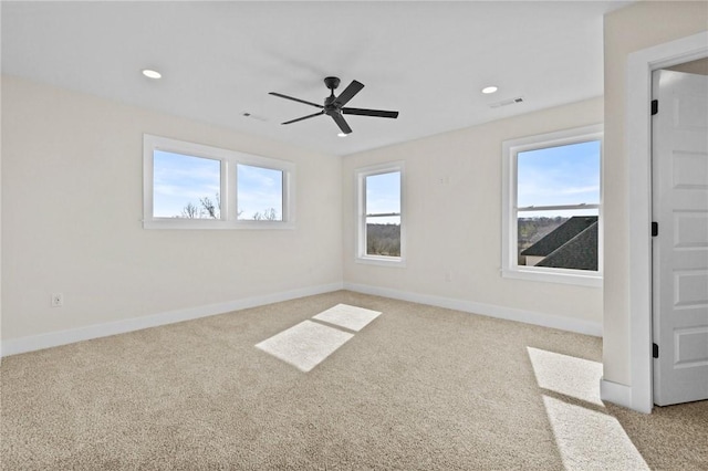 spare room featuring a wealth of natural light, light colored carpet, visible vents, and baseboards