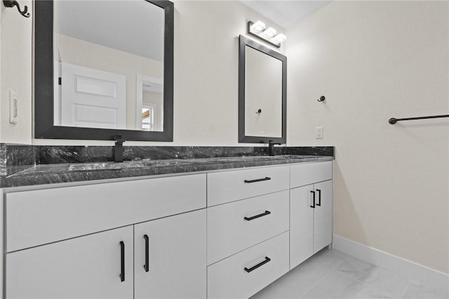 full bathroom featuring marble finish floor, double vanity, a sink, and baseboards