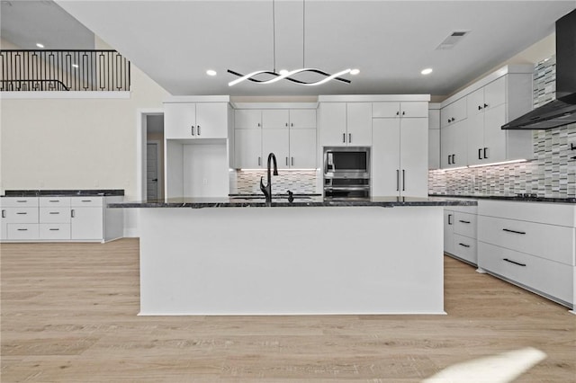 kitchen with a kitchen island with sink, wall chimney exhaust hood, appliances with stainless steel finishes, and white cabinetry