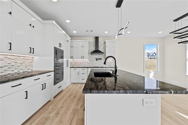 kitchen with a sink, hanging light fixtures, an island with sink, and wall chimney exhaust hood