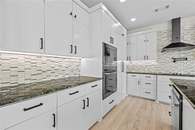 kitchen featuring visible vents, wall oven, white cabinets, built in microwave, and wall chimney exhaust hood