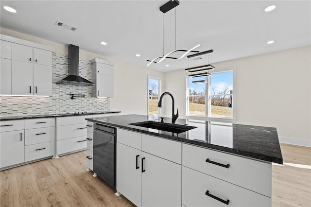 kitchen featuring dark stone countertops, wall chimney exhaust hood, a sink, and an island with sink