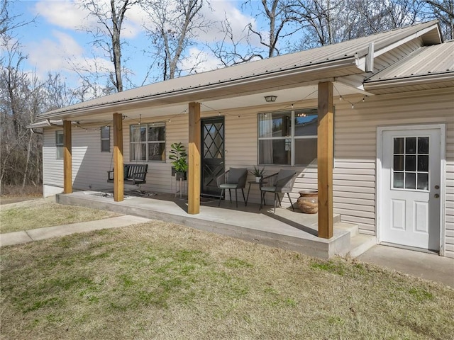 entrance to property with a porch, metal roof, and a lawn